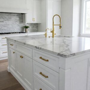 Modern white kitchen island with marble top accented with gold details.