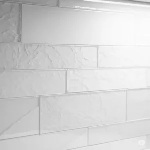 Close-up view of a subtly textured white on white kitchen backsplash, showcasing elegant variations in tone and finish.
