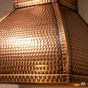 A detailed view of a hammered copper range hood, highlighting the unique, hand-worked texture of the copper kitchen hood vents that catches light beautifully and creates a one-of-a-kind look.