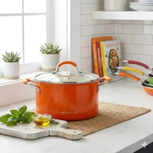 A lifestyle illustration showing a bright Rachael Ray orange pot used as a decorative accent in a white farmhouse kitchen.
