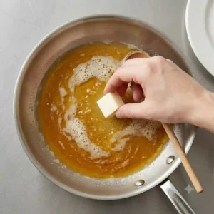 Swirling a cold cube of butter into a hot pan sauce off the heat to show how to cook with butter without burning.
